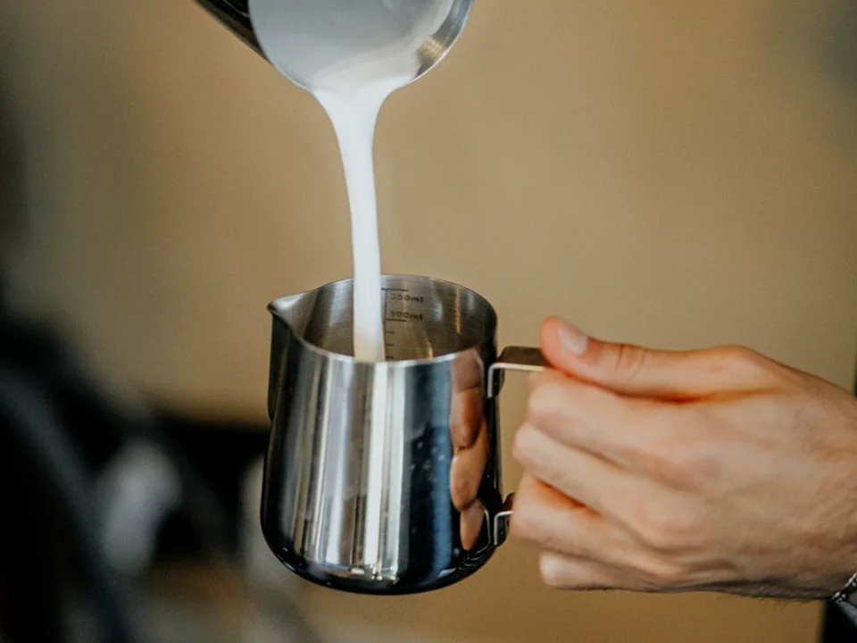 Cold milk being poured into a stainless steel frothing pitcher