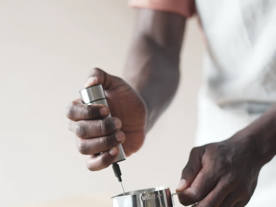 Hand frother held at the surface of milk in a metal pitcher