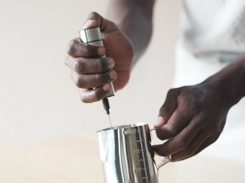 Hand frother mixing milk deeper in a stainless steel pitcher