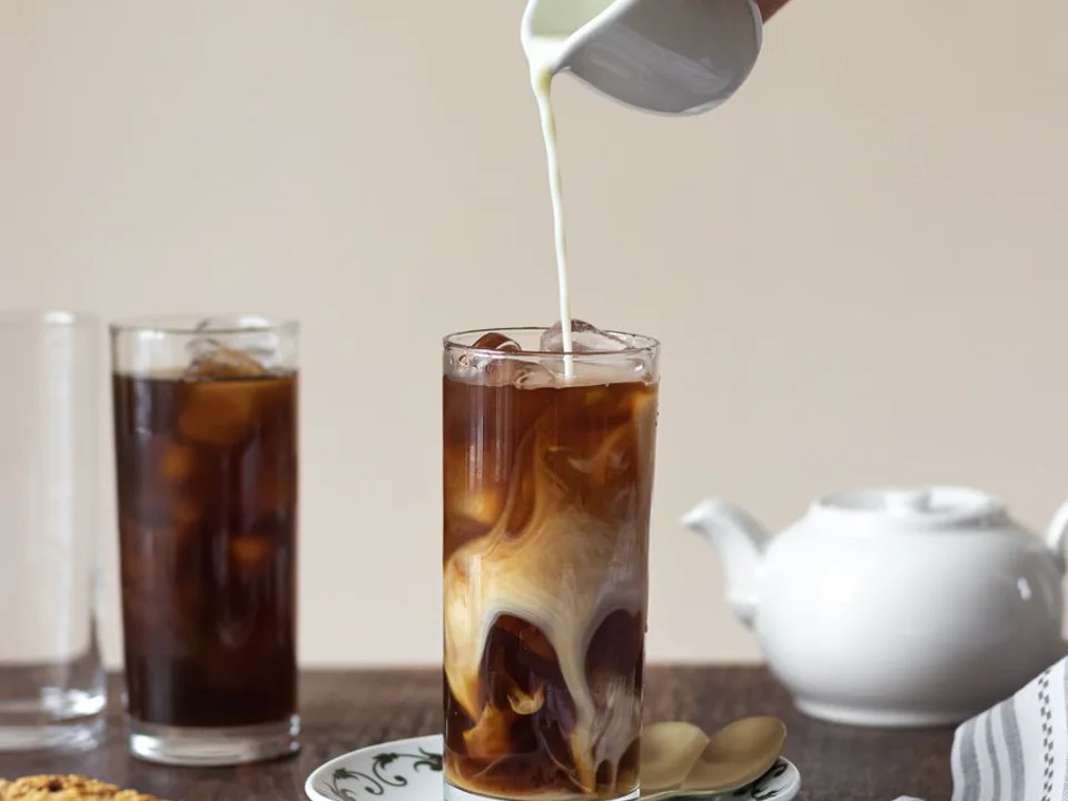 Cold foam being poured over a glass of iced coffee